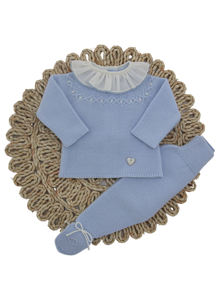 This two-piece babygrow from Artesania Granlei is a perfect design for baby boys and girls. The top has a delicate diamond pattern with white details and an ivory ruffle collar. Also, this beautiful to has a mother-of-pearl logo heart charm on the front. The matching pants have white knitted bows on the feet.