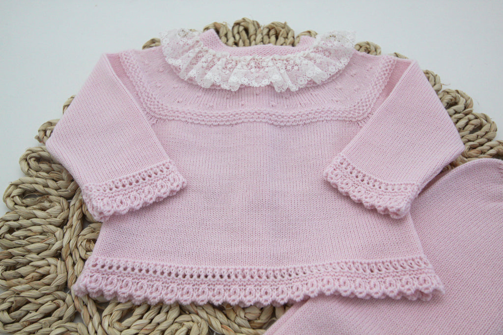 Pink two-piece set for newborn girls and boys by Artesania Granlei. This set has a beautiful top with a pretty white ruffle lace collar and scalloped trims. The pants have white bows on the feet.